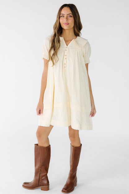 Young woman wearing an ivory short dress with a textured stripe with short puff sleeves and a V-neckline.