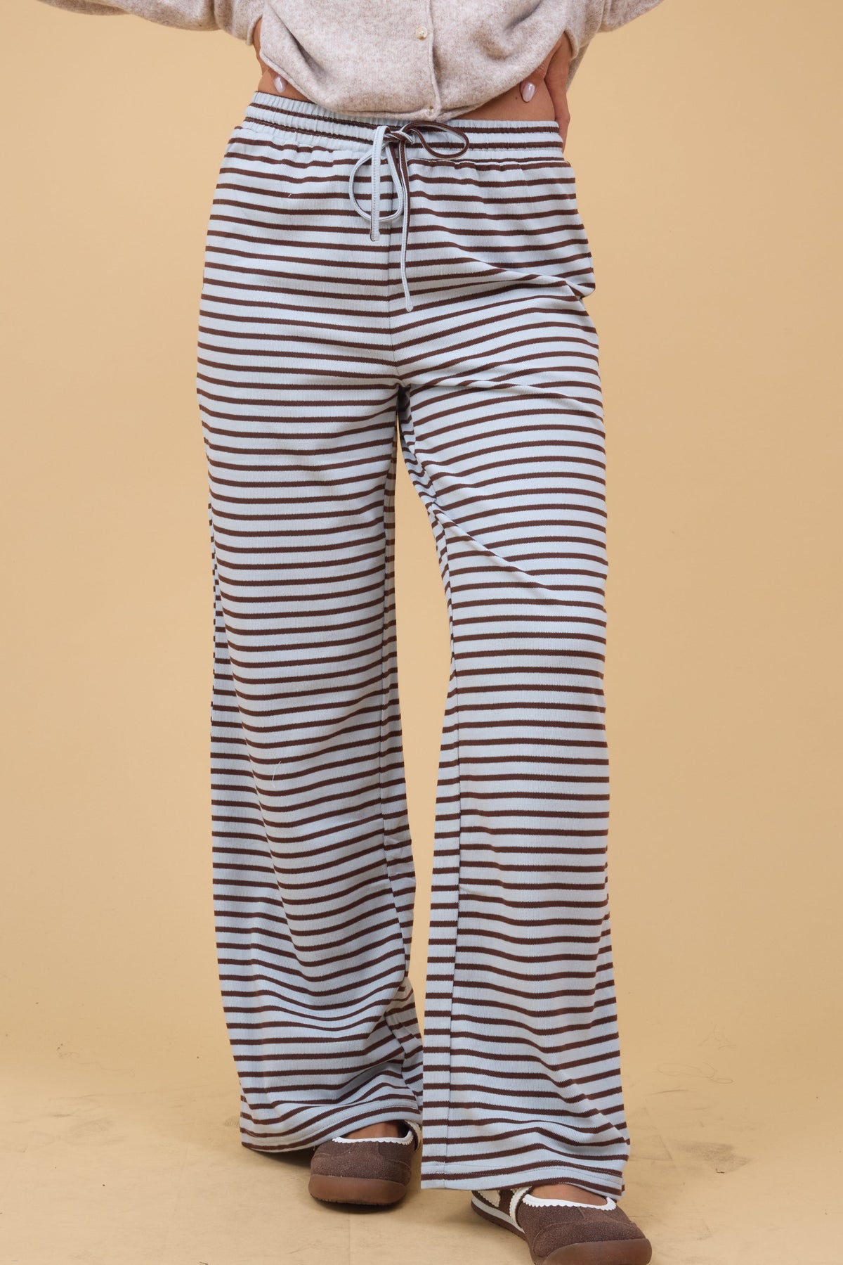 Woman wearing wide leg knit lounge pants in light blue and brown stripe with a wide elastic waist.