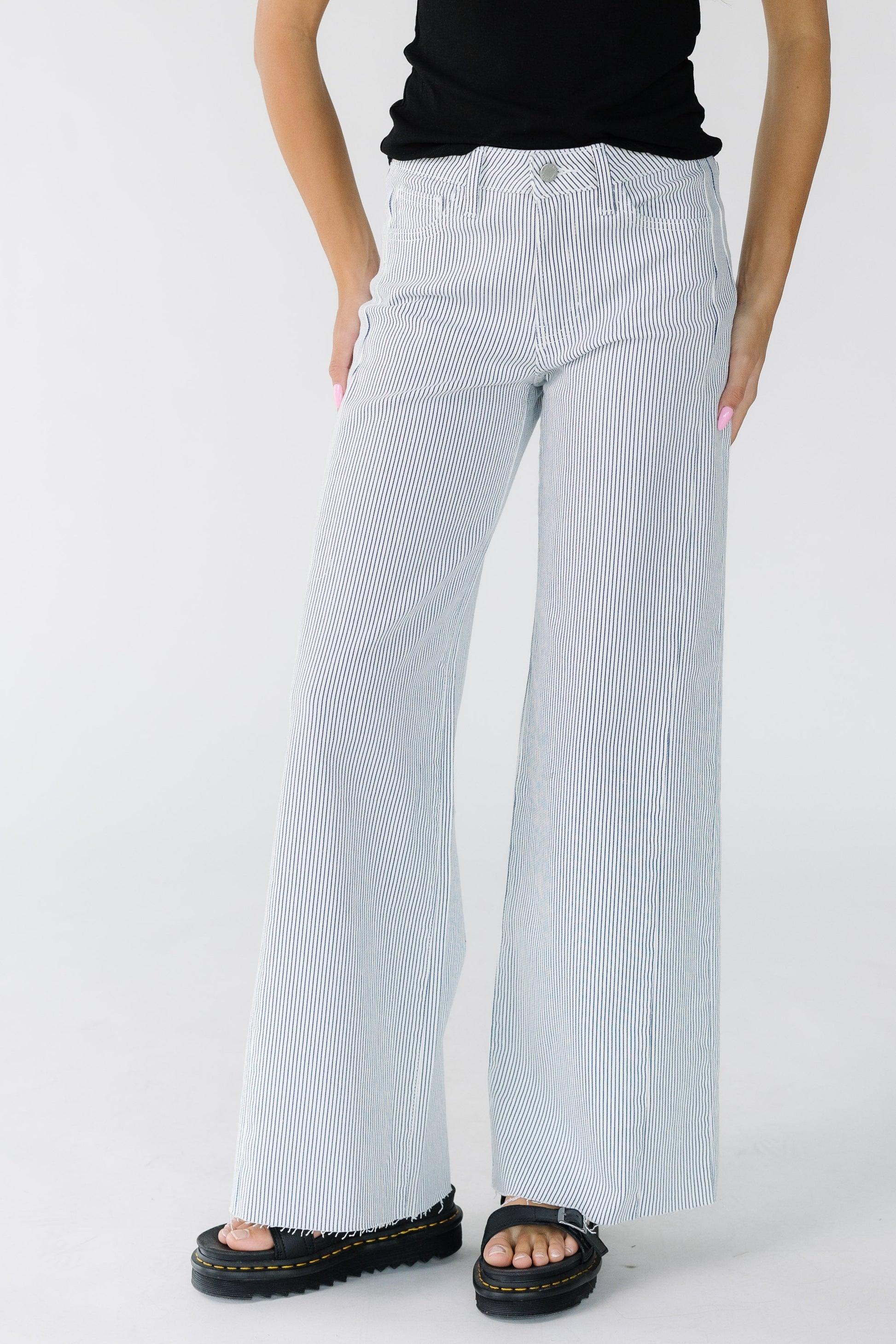 Woman wearing a pair of modest wide leg jeans in white with thin navy stripe with cut hems.