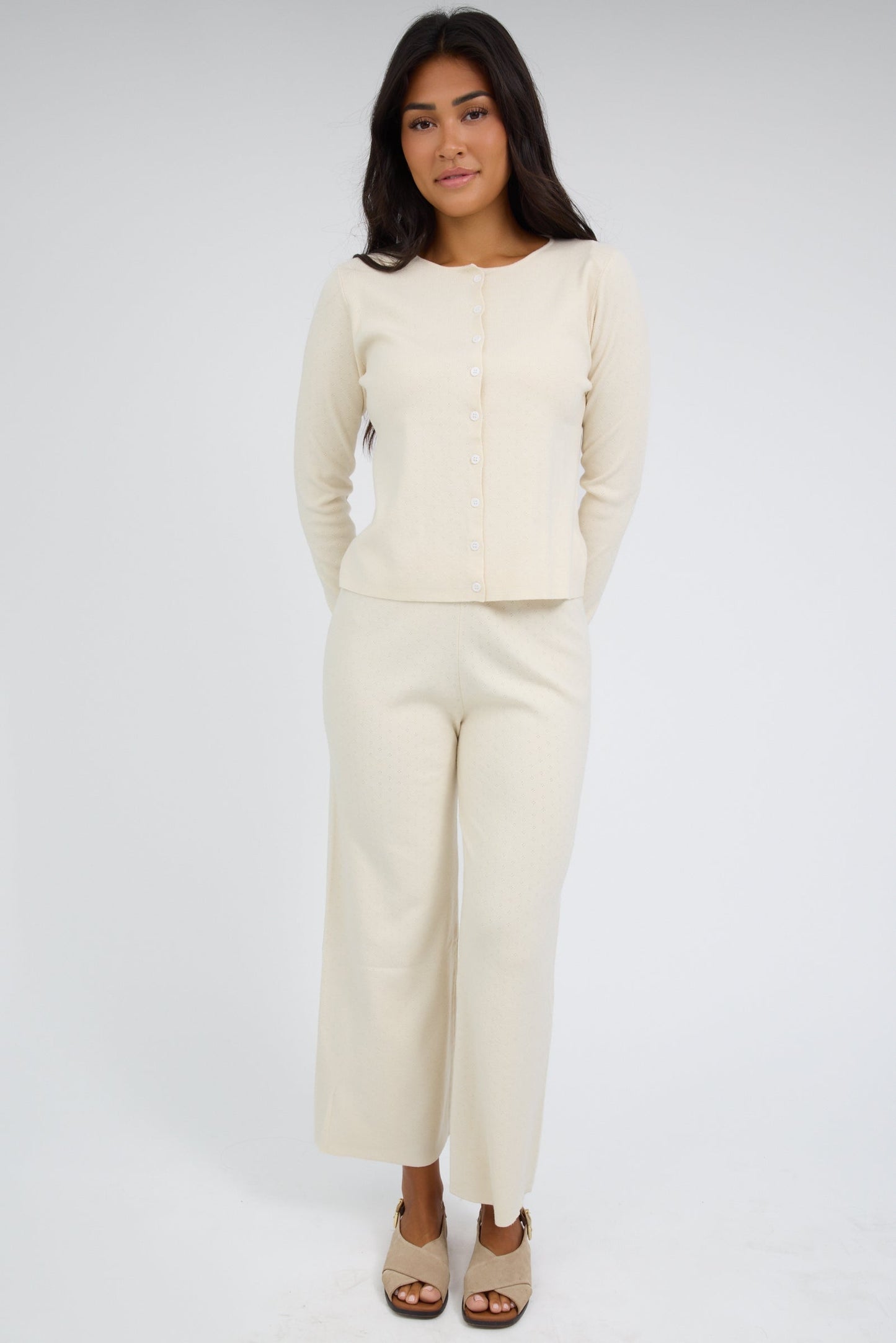 Young woman wearing a cream color 2 piece set with a button down cardigan with long sleeves and wide leg pant.