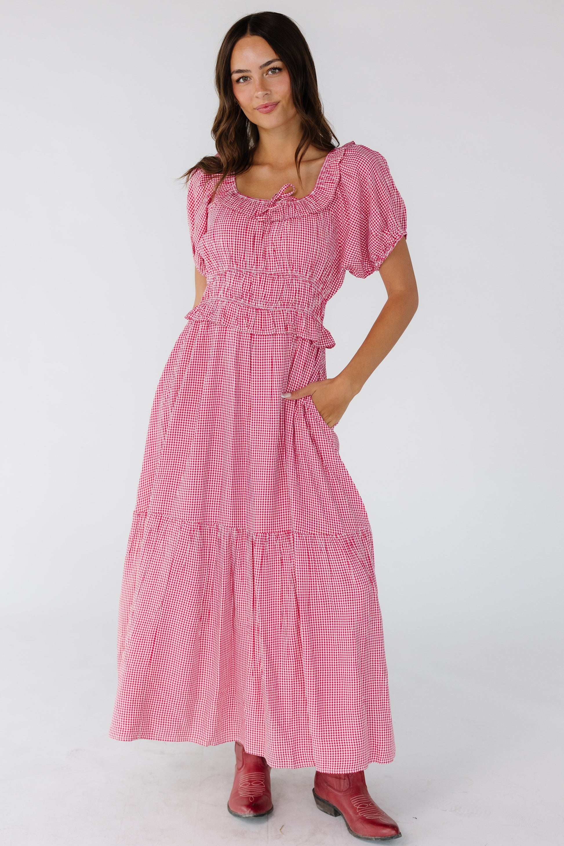 Young woman wearing a red & white gingham midi dress with a ruffled scoop neckline, short puff sleeves and side pockets.