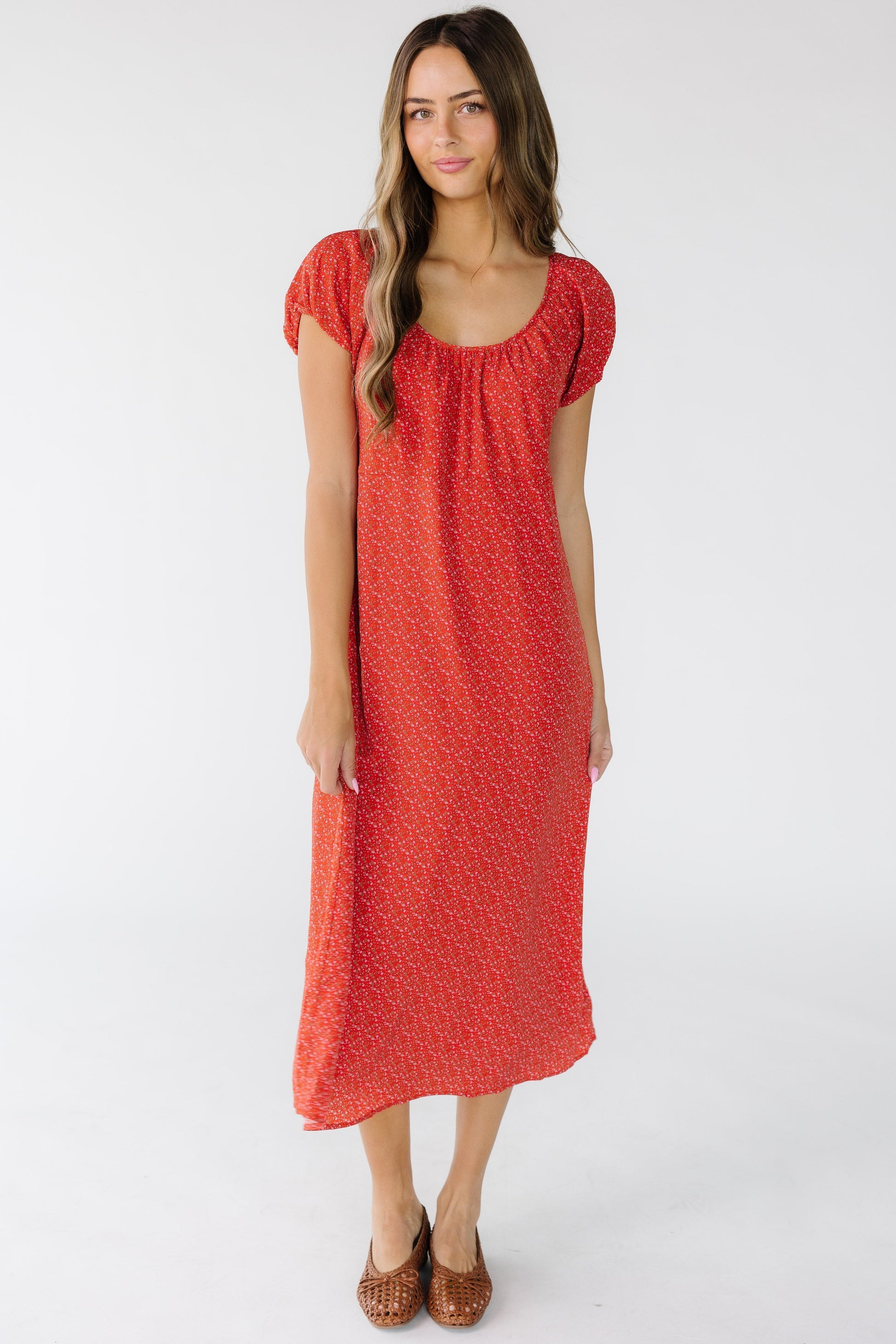 Young woman wearing a loose fitting column midi dress with short puff sleeves and a wide scoop neckline.