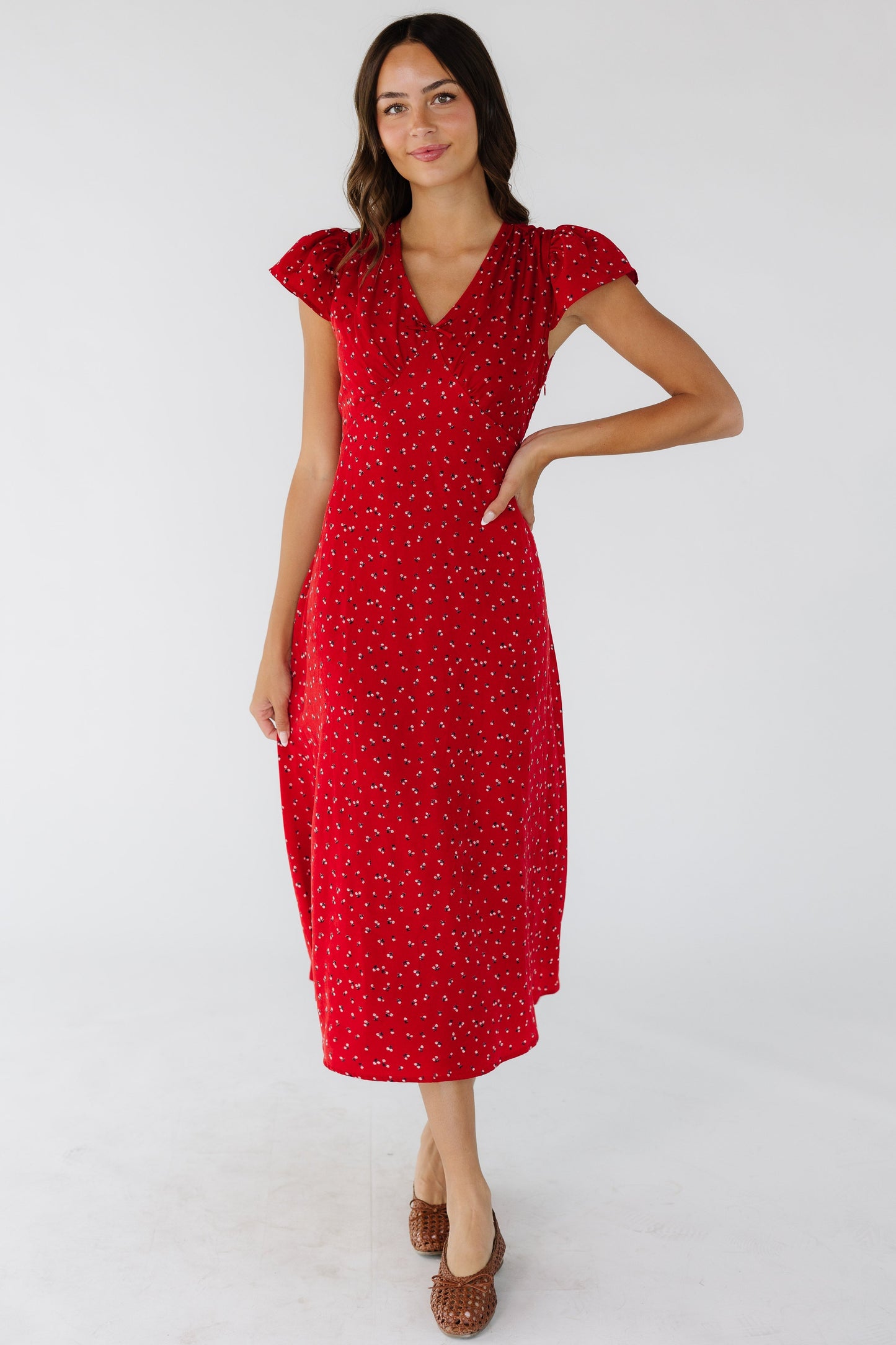 Woman wearing a red floral midi dress with a V-neckline, short flutter sleeves and a pointed empire waist.