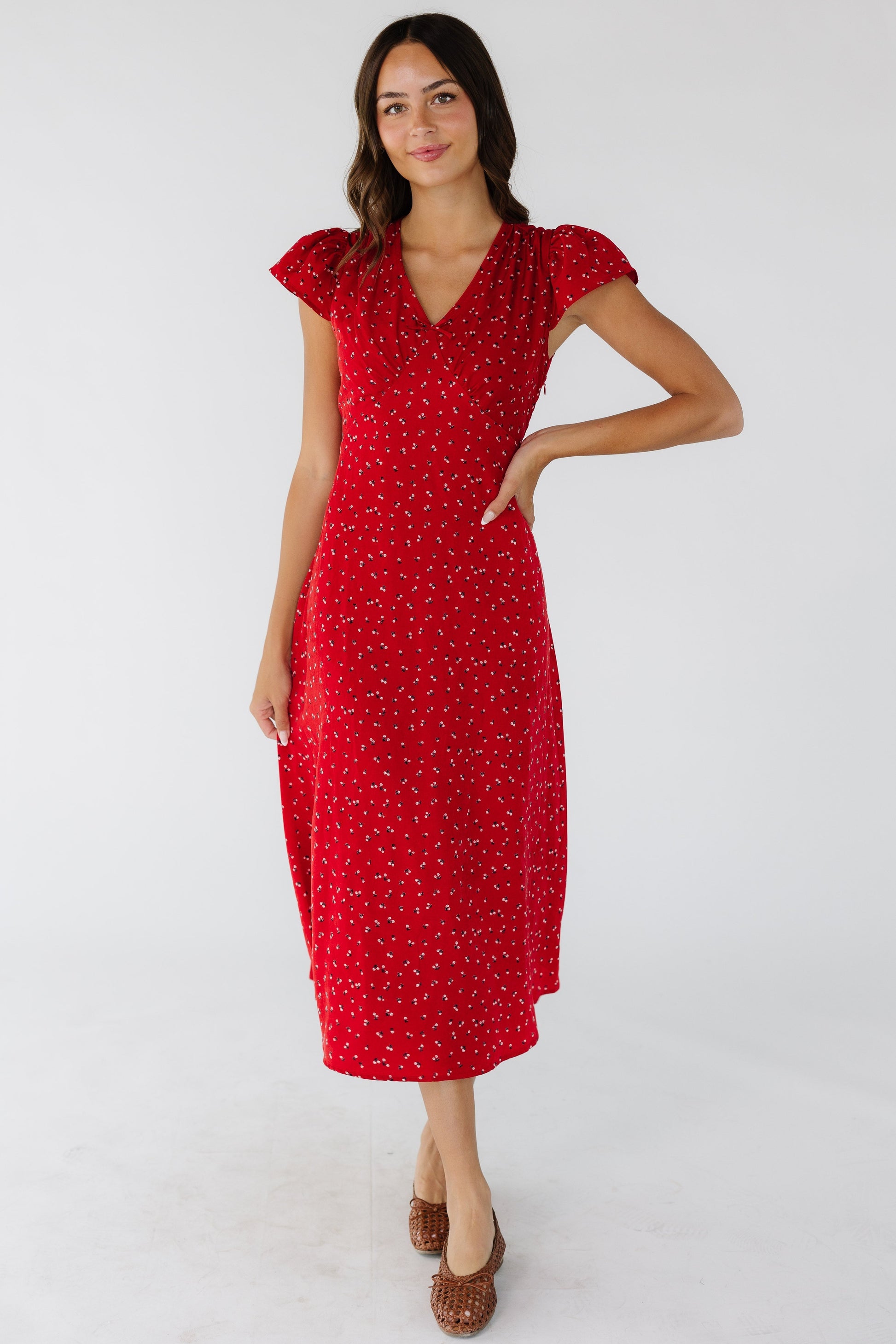 Woman wearing a red floral midi dress with a V-neckline, short flutter sleeves and a pointed empire waist.