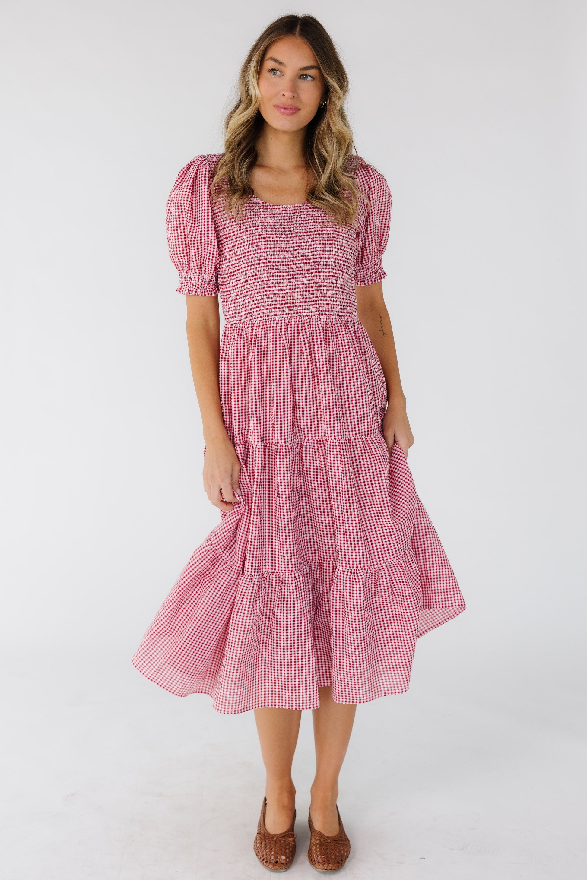 Woman wearing a red & white gingham midi dress with a smocked front & back bodice and short puff sleeves.
