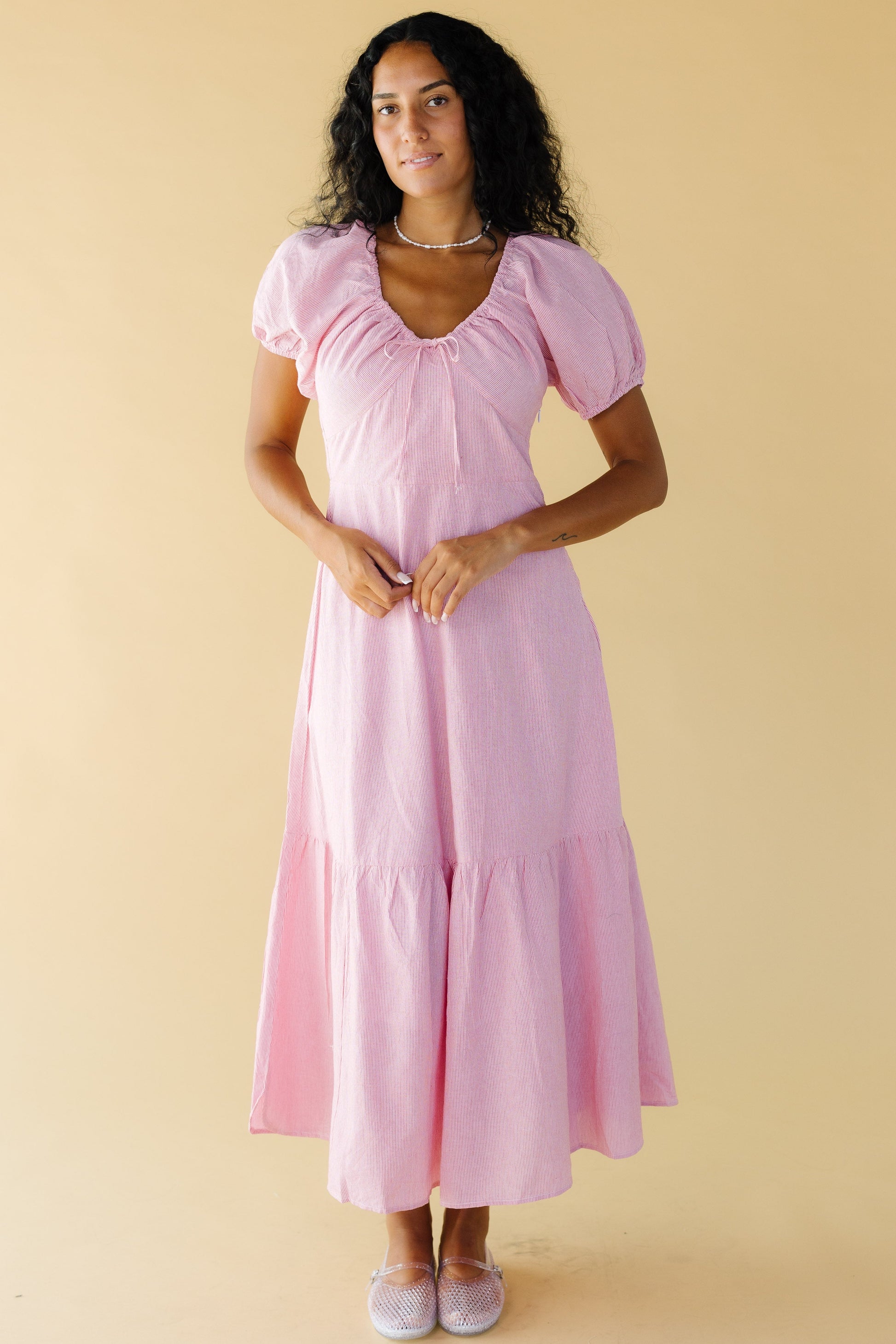 Woman wearing a very narrow red & white stripe midi-maxi dress with a close fitting bodice and a wide full skirt with a wide bottom ruffle.