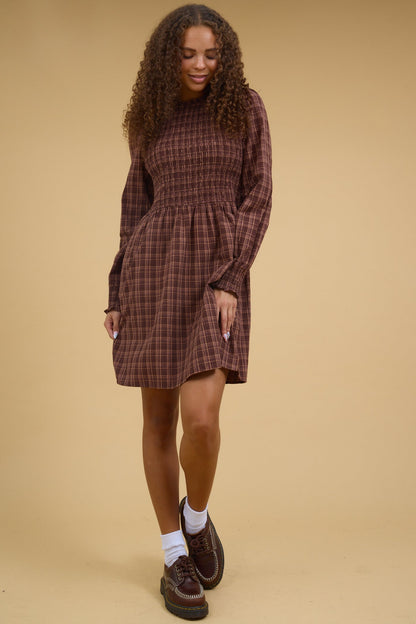 Young woman wearing a modest brown plaid short dress with a smocked bodice and long sleeves.