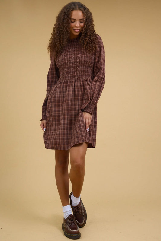 Young woman wearing a modest brown plaid short dress with a smocked bodice and long sleeves.