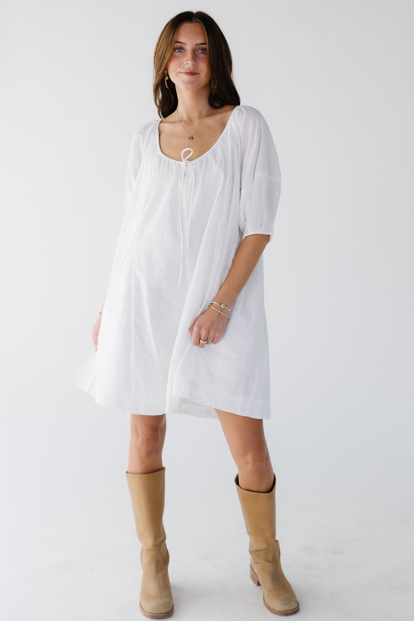 Woman wearing a white eyelet tunic dress with elbow length elbow sleeves and a drawstring scoop neckline.