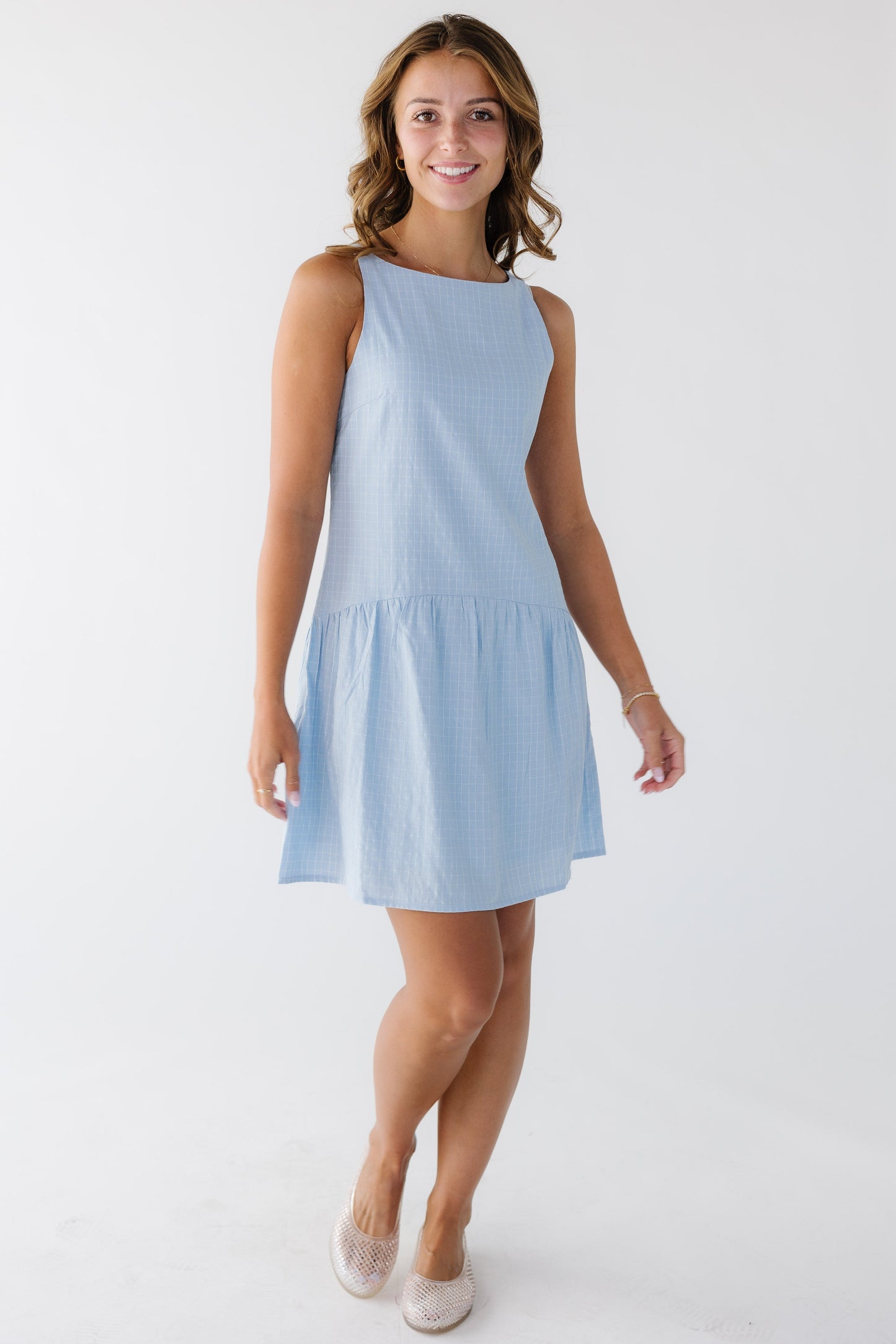 Young woman wearing a classy blue plaid sleeveless dress hemmed above the knee and a drop waist.