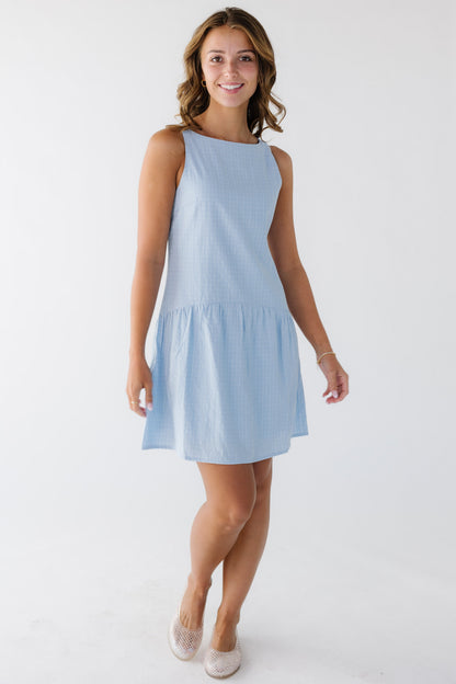 Young woman wearing a classy blue plaid sleeveless dress hemmed above the knee and a drop waist.
