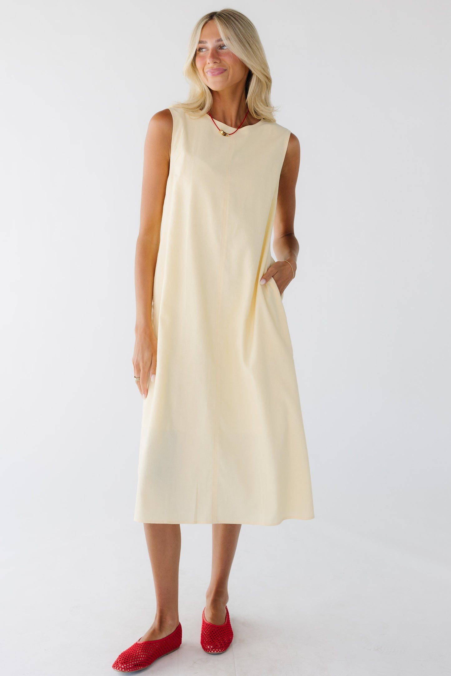 Young woman wearing a yellow sleeveless midi dress with side pockets
