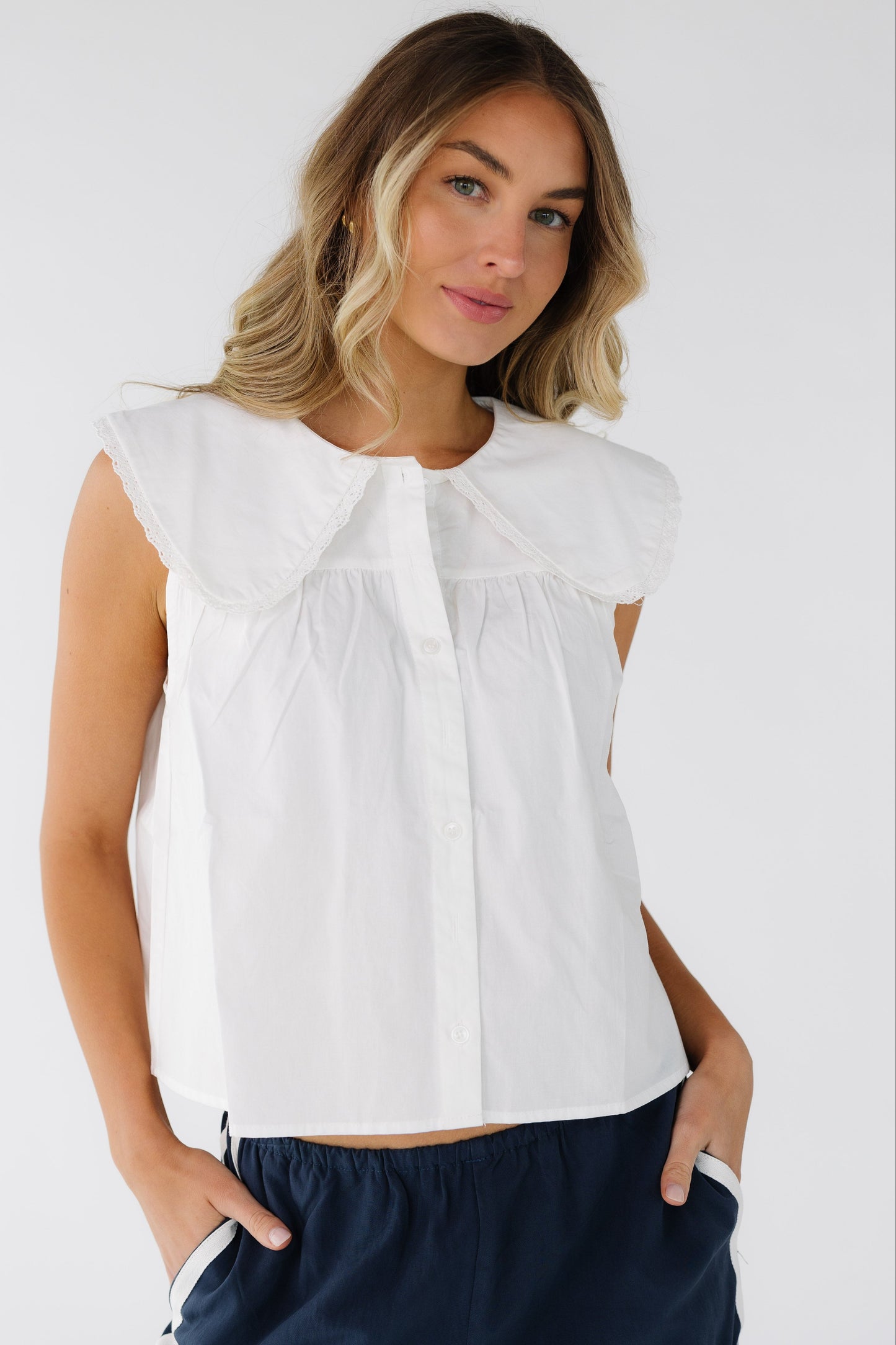 Woman wearing a white sleeveless, button down blouse with a wide lace trimmed collar.