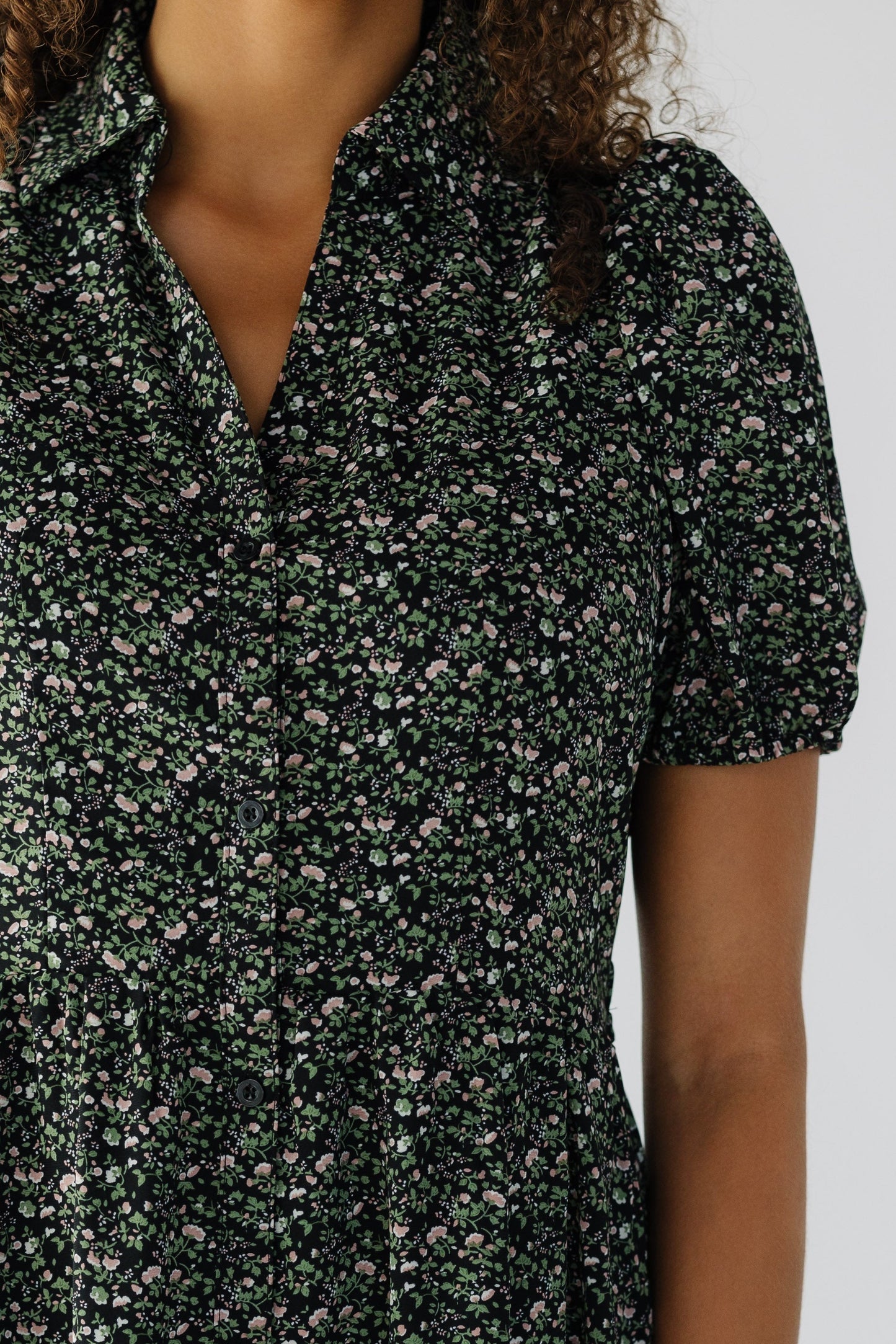 Close view of a teenage girl wearing a black floral, button down dress with short puff sleeves.
