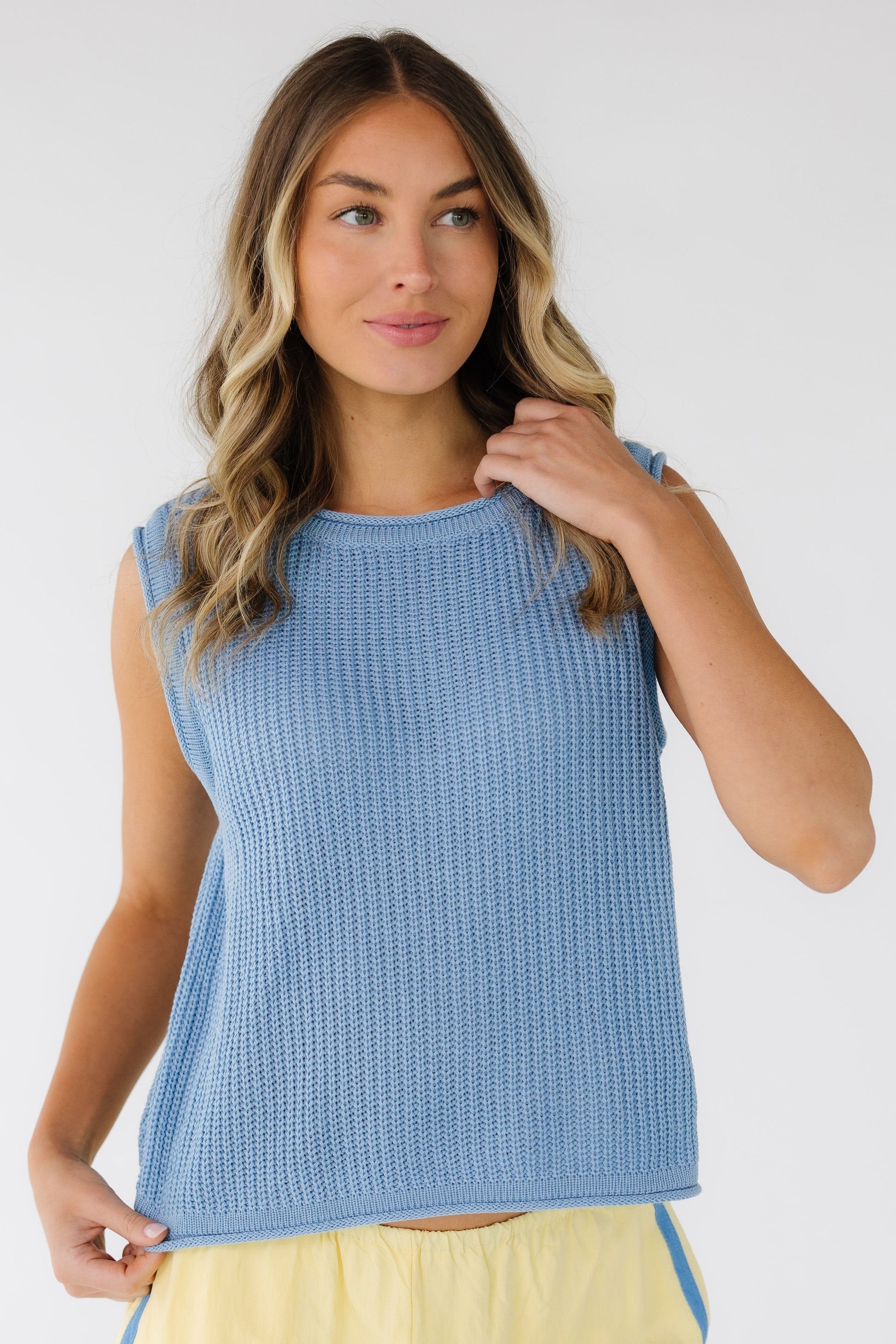 Woman wearing a light blue rib knit sleeveless sweater vest with rolled hems.
