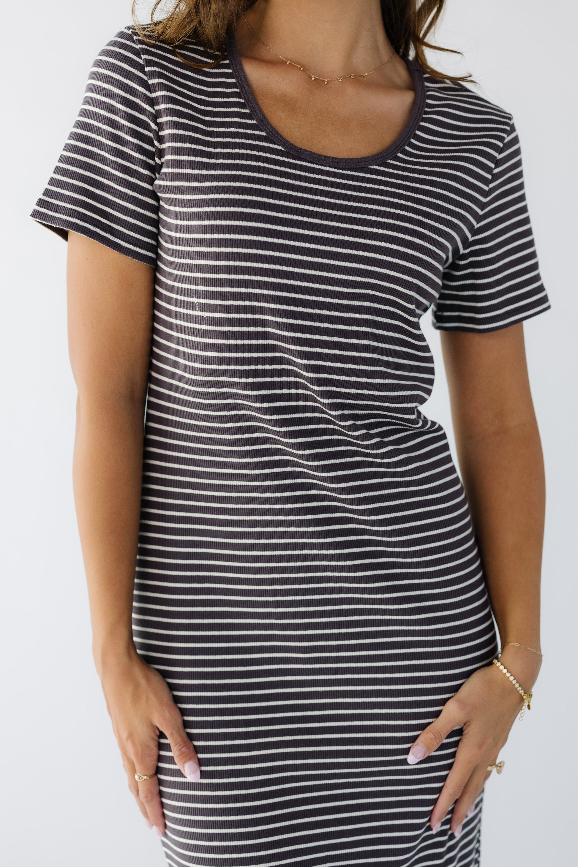 Close up view of a woman wearing a close fitting, stretchy  rib knit dress with a scoop neckline and short sleeves.