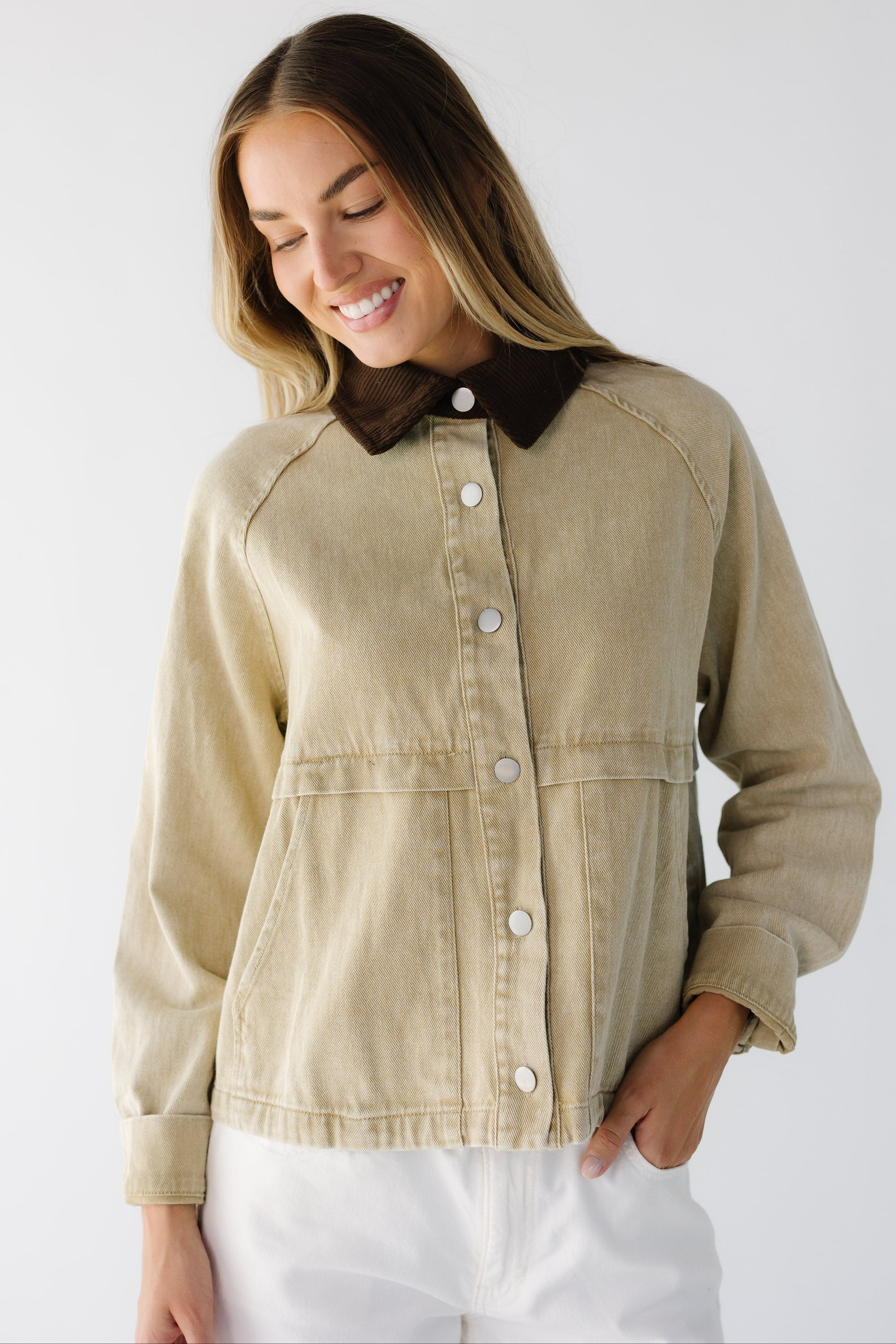 Woman wearing a tan jacket with large front pockets, metal buttons, long sleeves and a brown corduroy collar.