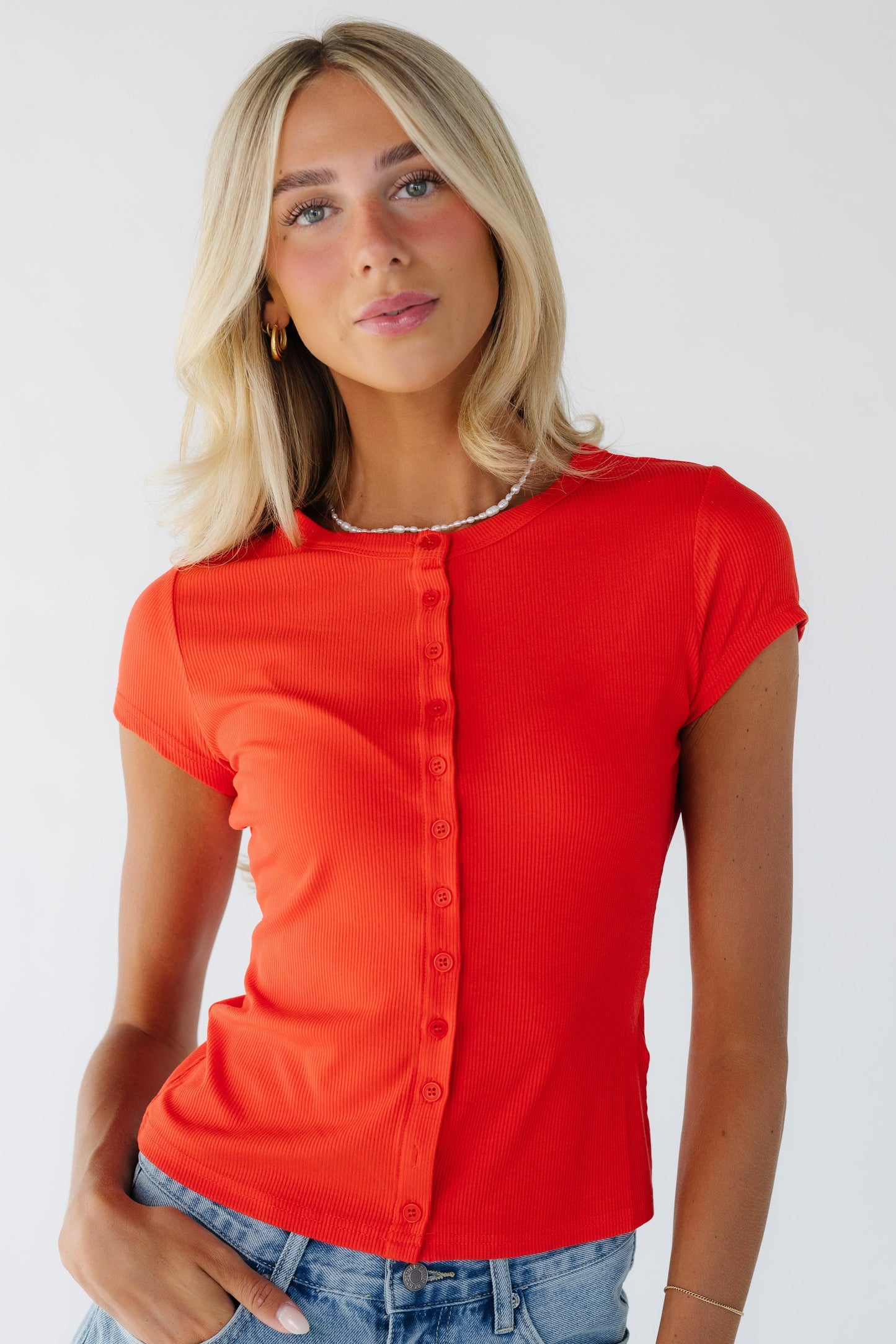 Young woman wearing a modest red button down top with a round neckline and short sleeves.