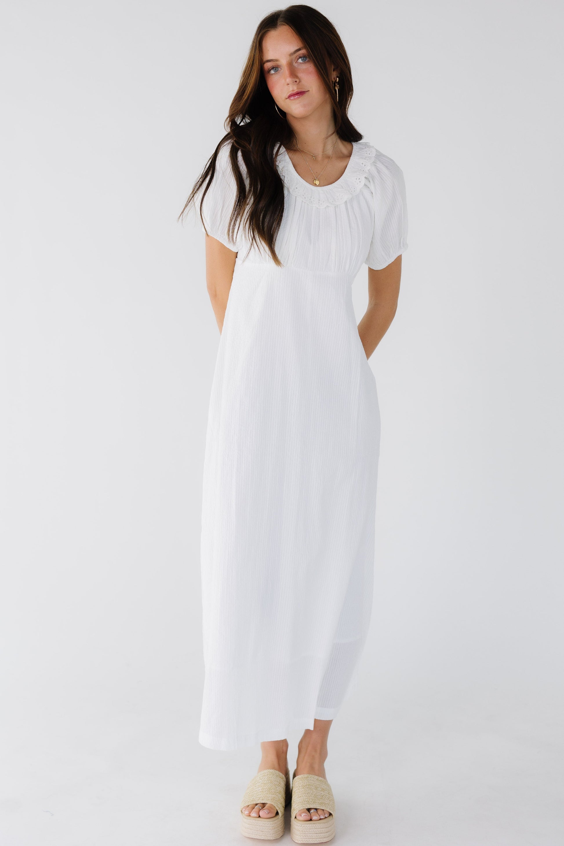 Closer fitting A-line skirt midi dress  worn by a young woman with an empire waist, gathered bodice, eylet trimmed scoop neckline and short puff sleeves.