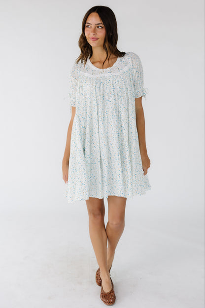 Young woman wearing a white and blue floral dress with short sleeves and a round neckline. 