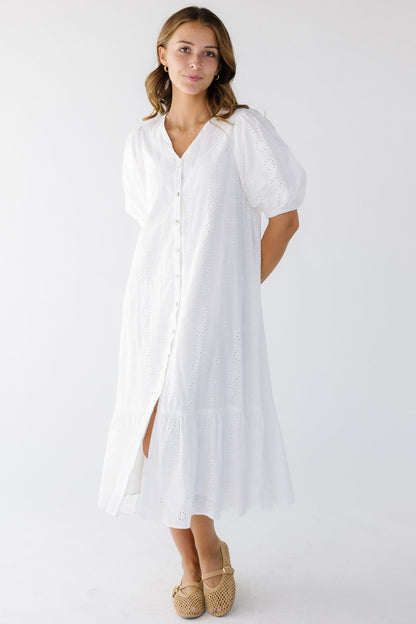 Young woman wearing a a loose fitting midi dress in white eyelet with a wide bottom ruffle that buttons down the front.