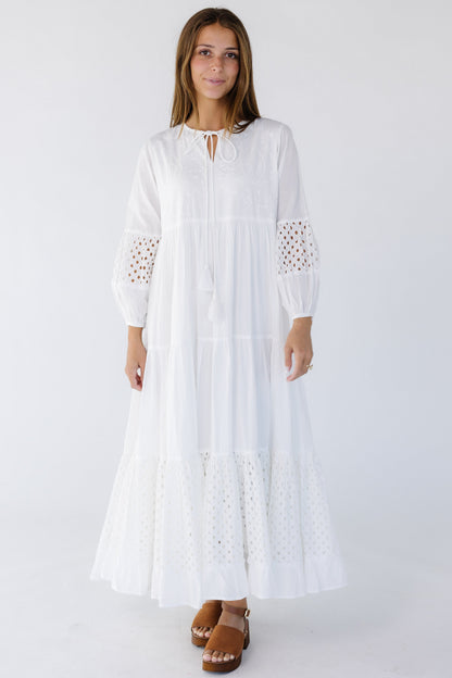 Woman wearing a white tiered maxi dress with eyelet tiers and eyelet sleeve   sections, long sleeves and round neckline.