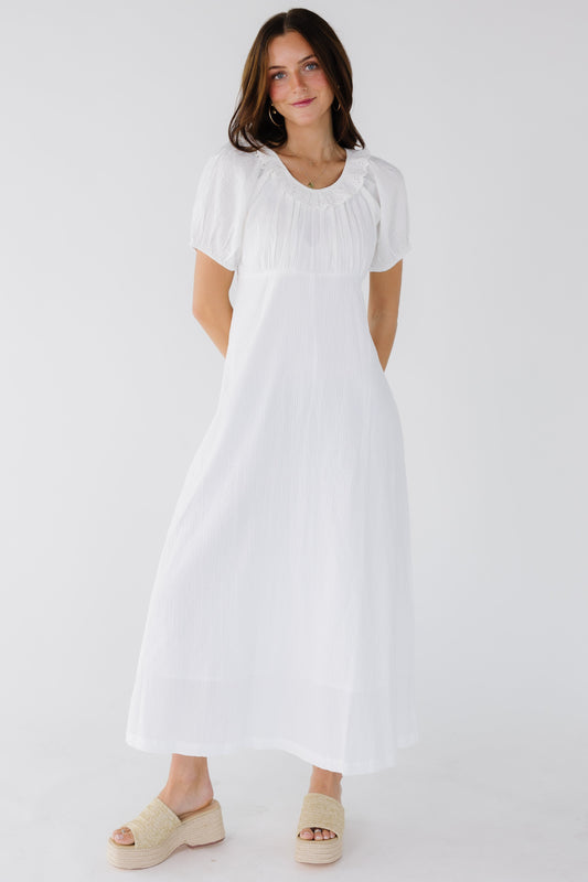 Young woman wearing a white on white stripe midi dress with scoop neckline with eyelet trim and short puff sleeves.