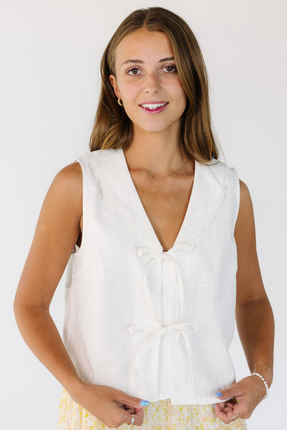 Woman wearing a white sleeveless top with a 2 tie closure and a V-neckline with a lace edge shawl collar.
