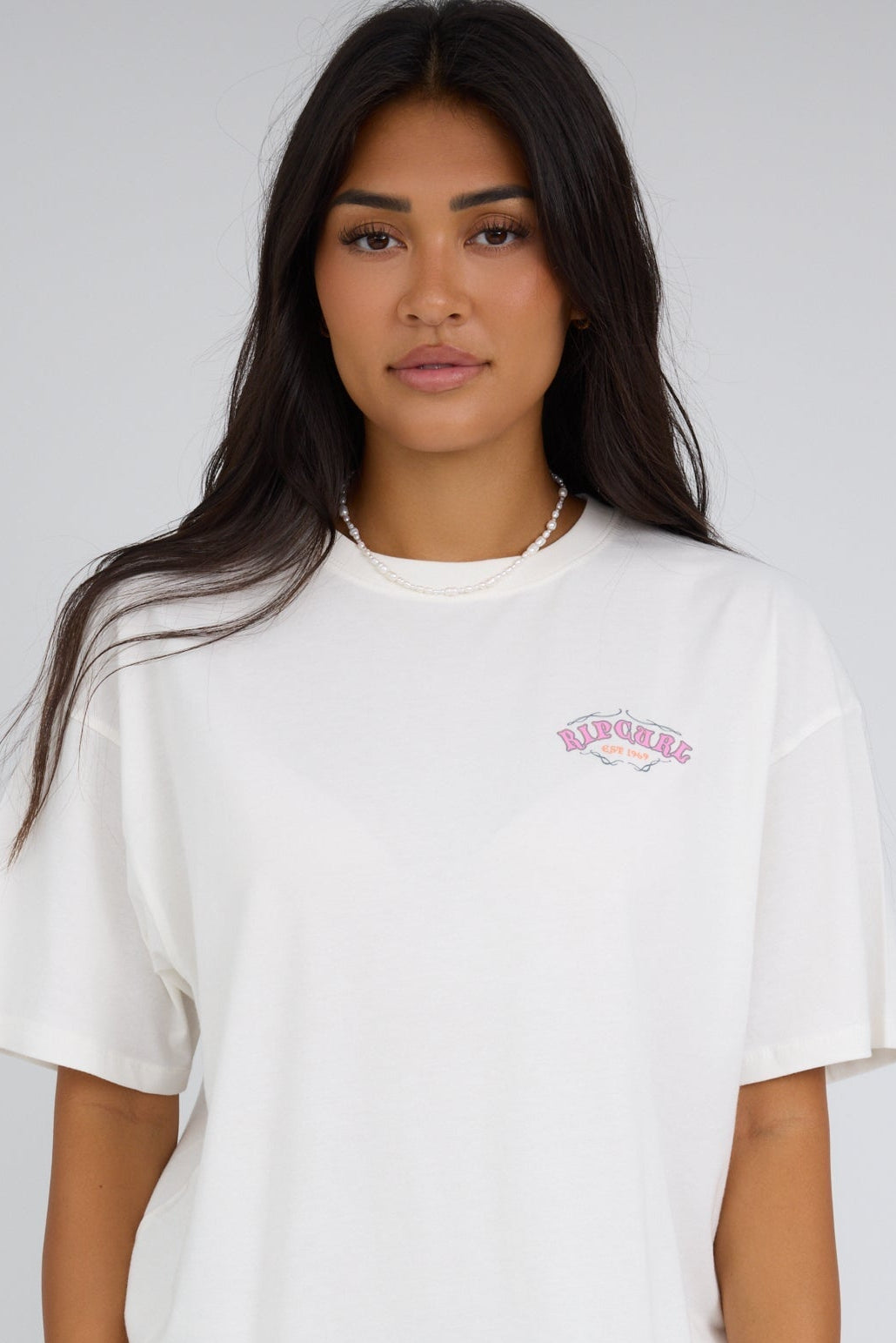 Woman wearing a white loose fitting graphic tee by Rip Curl.