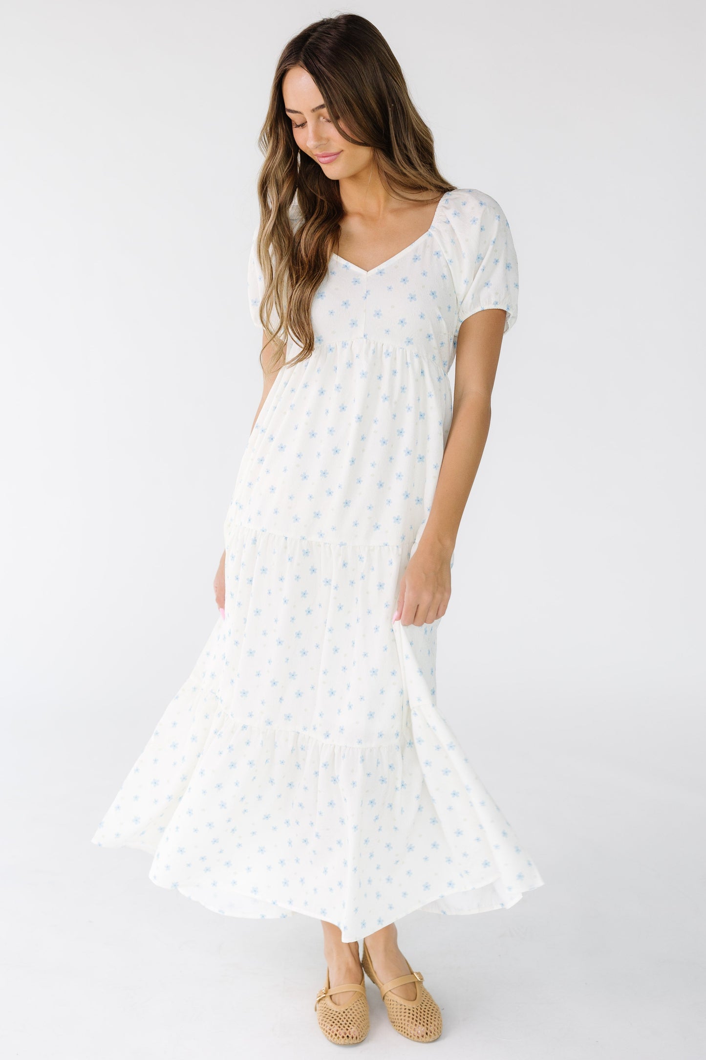 Woman wearing a modest white midi-maxi dress with blue floral print with multiple tier dress with short sleeves and a sweetheart neckline.