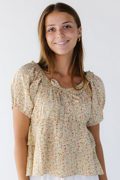 Woman wearing a yellow floral print blouse with short puff sleeves, a wide ruffled neckline, empire waist and a double ruffle bottom.
