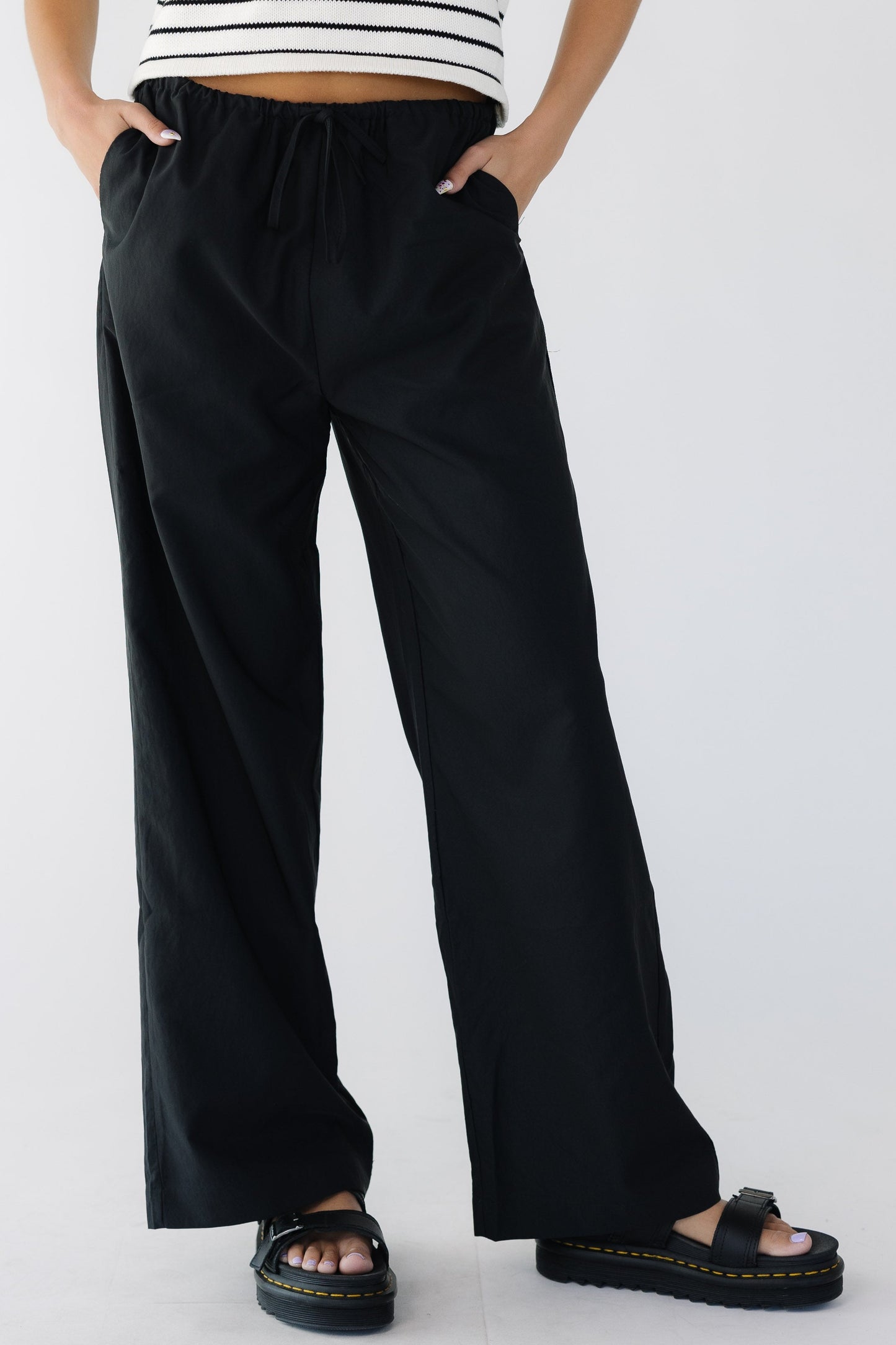 Young woman wearing a  modest pair of black wide leg pant with side pockets and elastic & drawstring waistband.