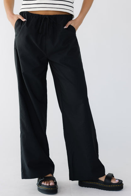 Young woman wearing a  modest pair of black wide leg pant with side pockets and elastic & drawstring waistband.