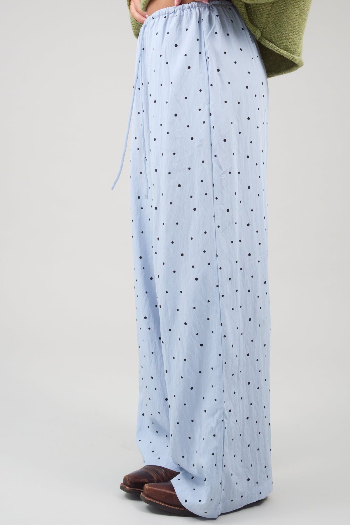 Side view of a woman wearing a wide leg pair of woven light blue and black polka dot pants.
