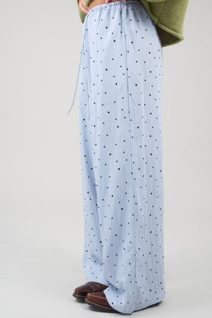 Side view of a woman wearing a wide leg pair of woven light blue and black polka dot pants.