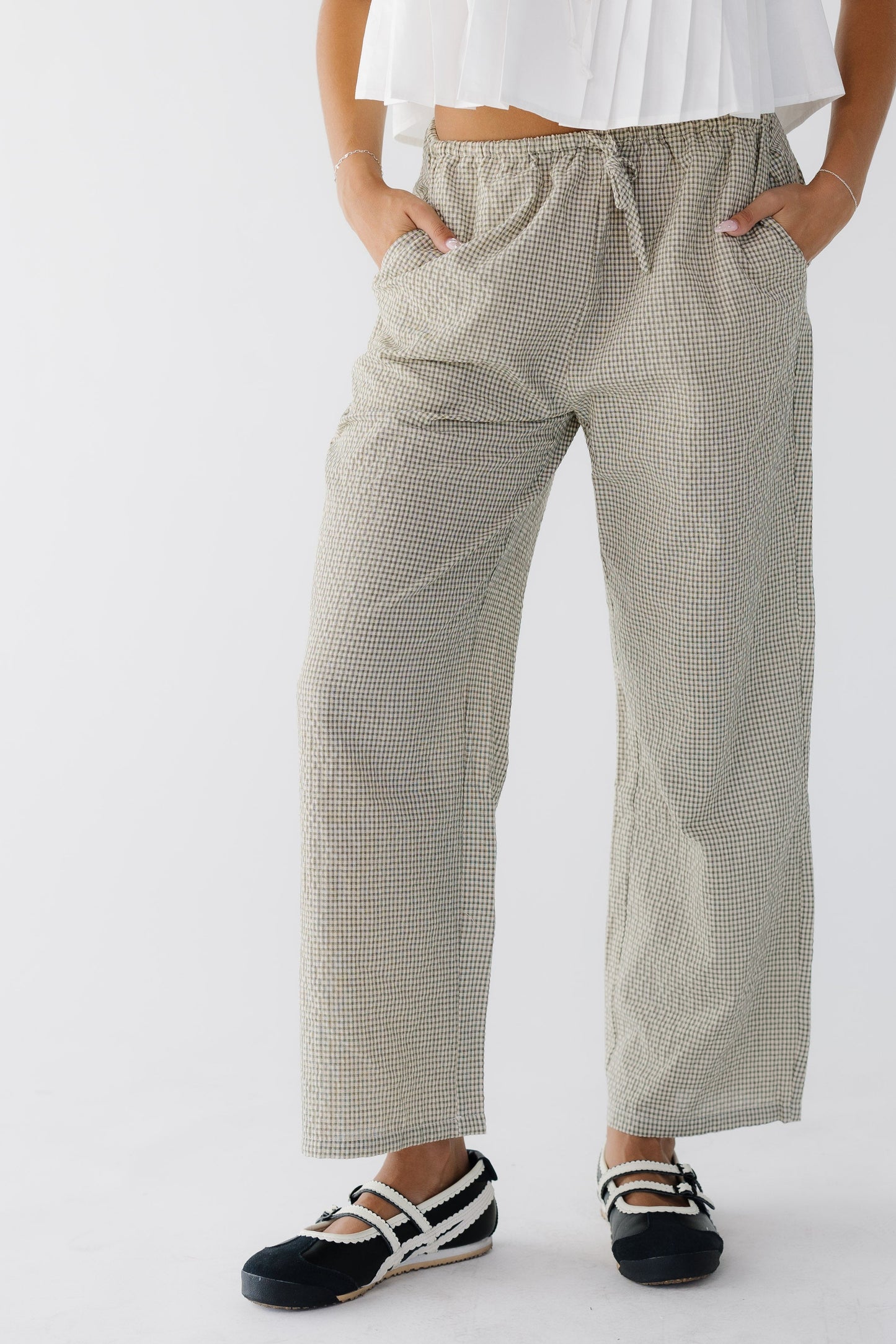 Young woman wearing loose fitting gingham woven pants in brown and white with side pockets.