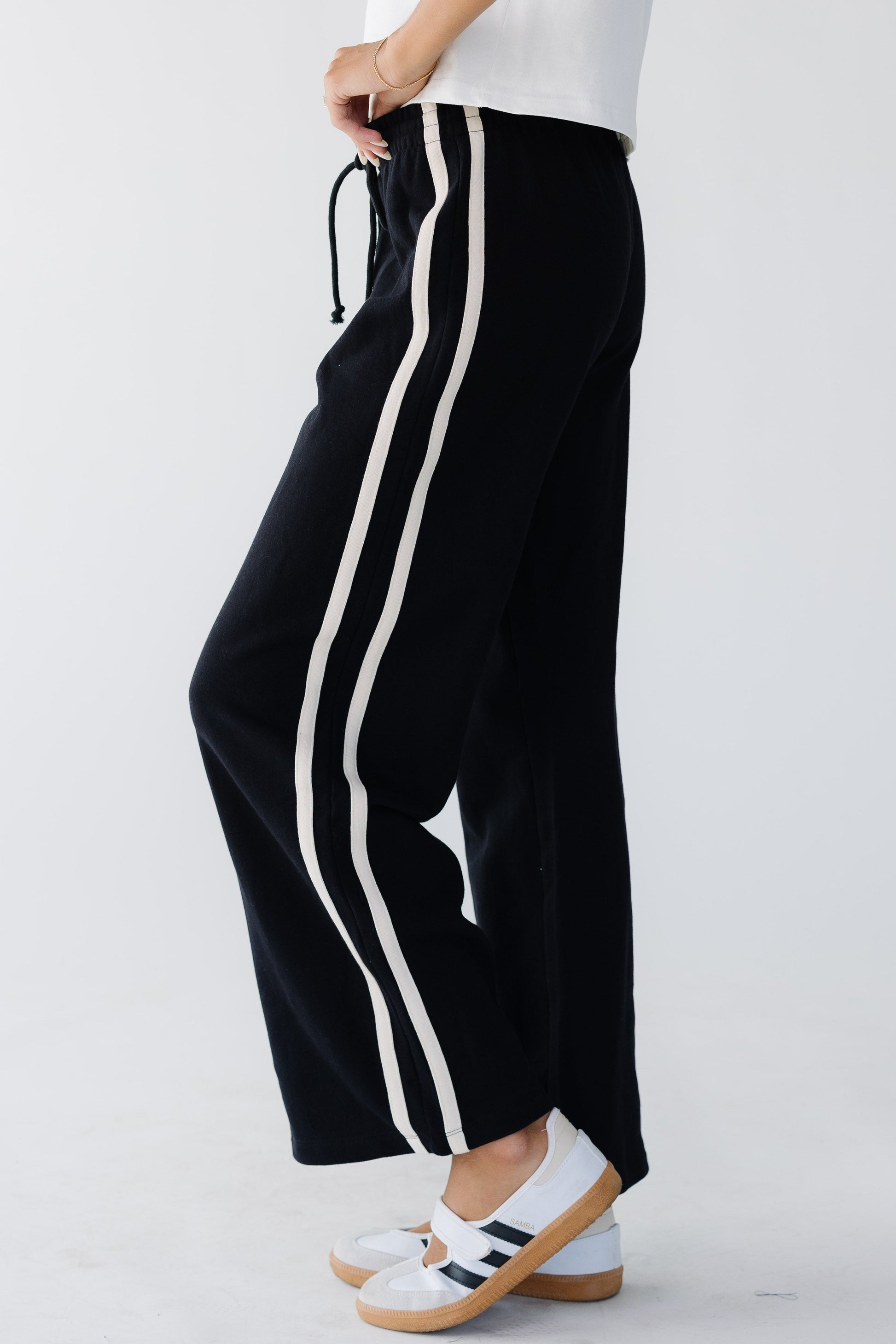 Woman wearing wide cut lounge pants with 2 white stripes down the leg and an elastic & drawstring waistband.