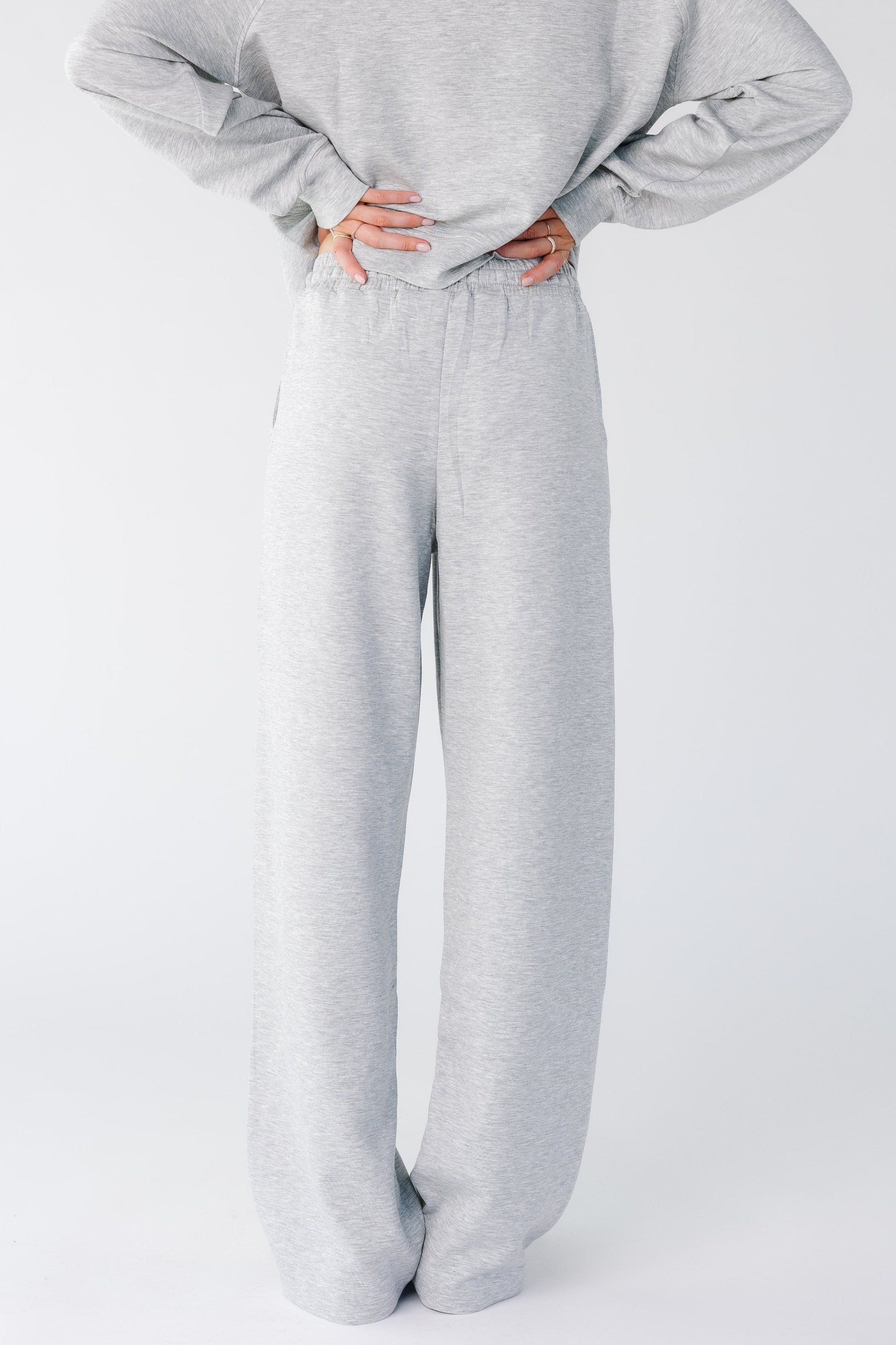 Back view of a woman wearing a pair of heather grey lounge pants with elastic waist and wide cut leg