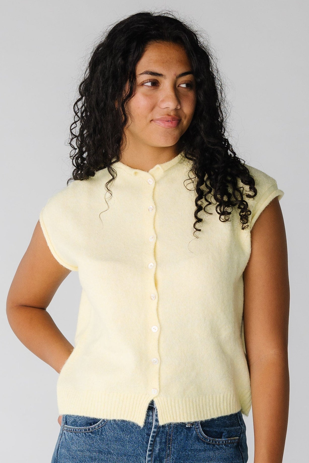 Woman wearing a sleeveless light yellow button down sweater vest.