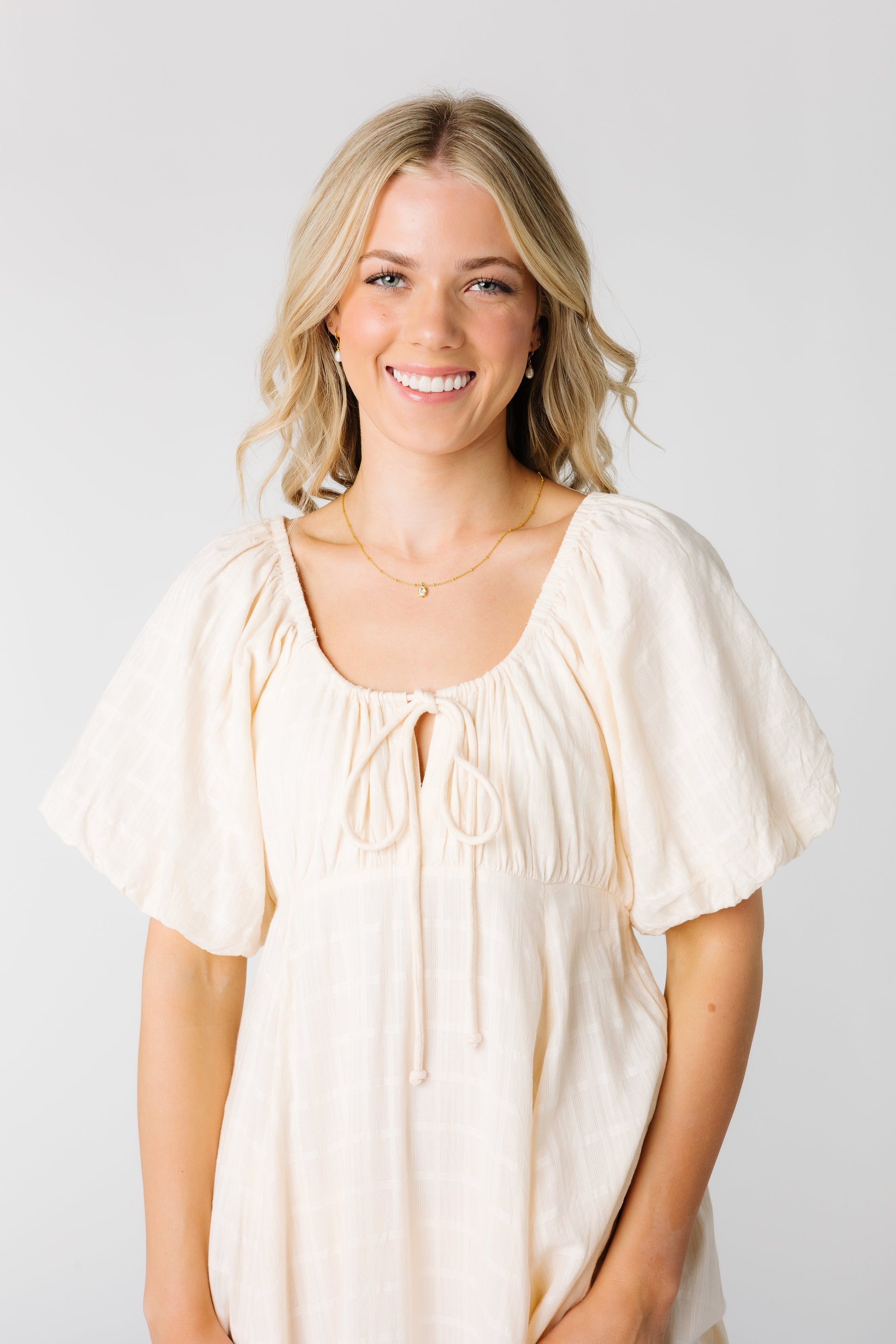 Close view of a woman wearing a cream dress with scoop neckline and short sleeves