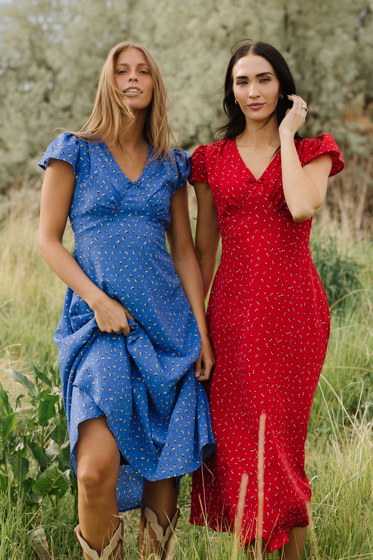 Two young woman wearing blue and red floral dresses with short flutter sleeves and a V-neckline.