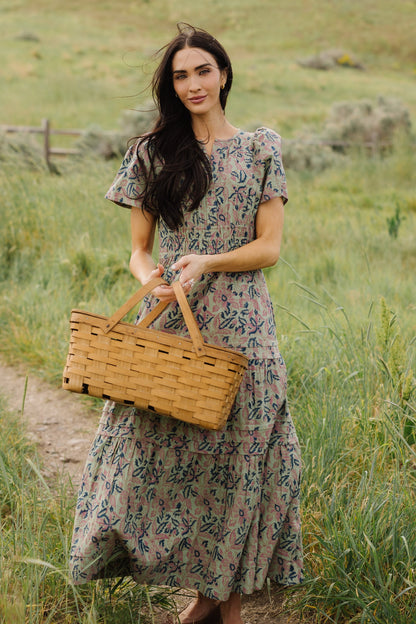 Young woman wearing a modest grean floral midi-maxi dress with short sleeves and a tiered and gathered skirt.