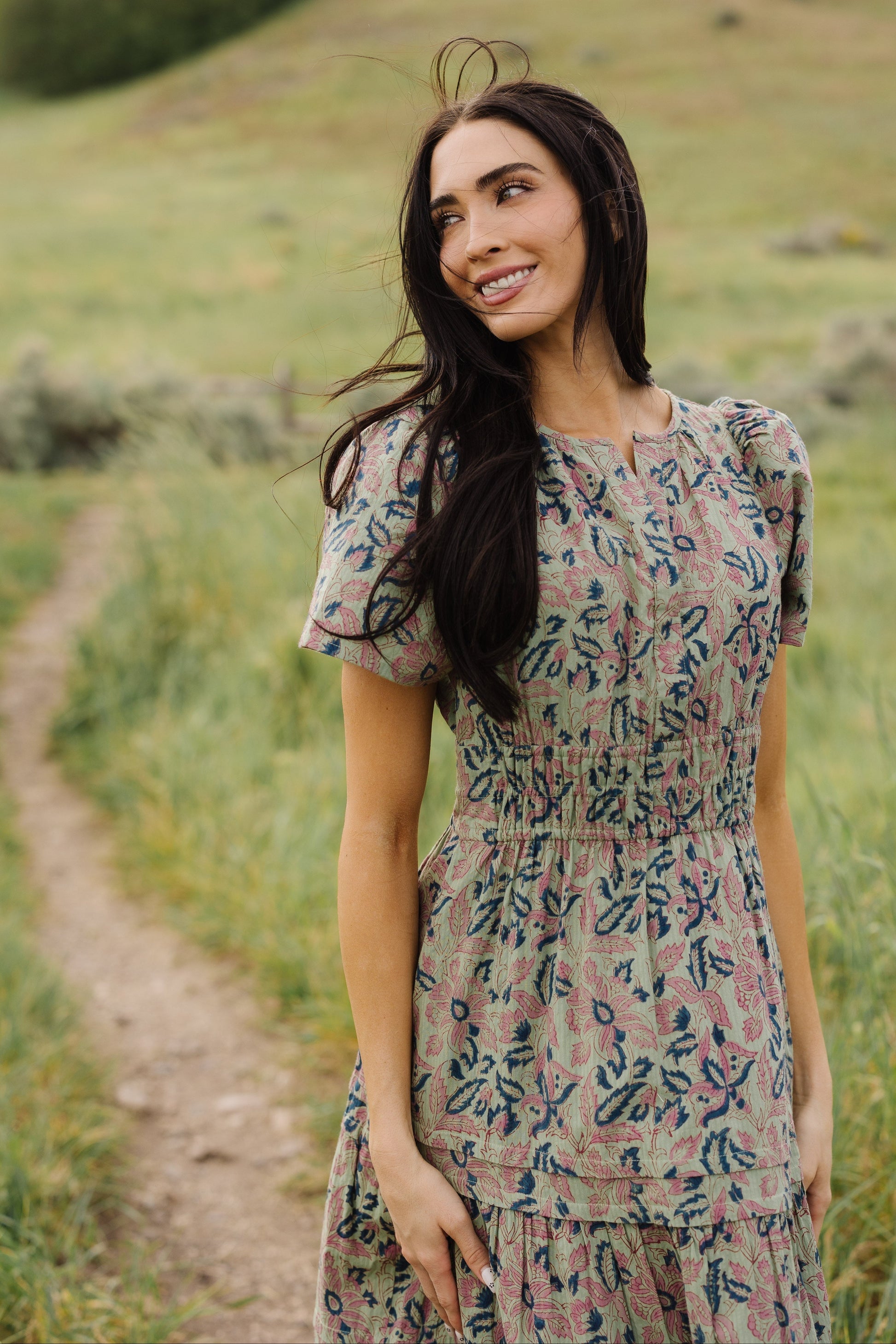 Woman wearing a green floral & paisley dress wtih gathered tieres and short sleeves.