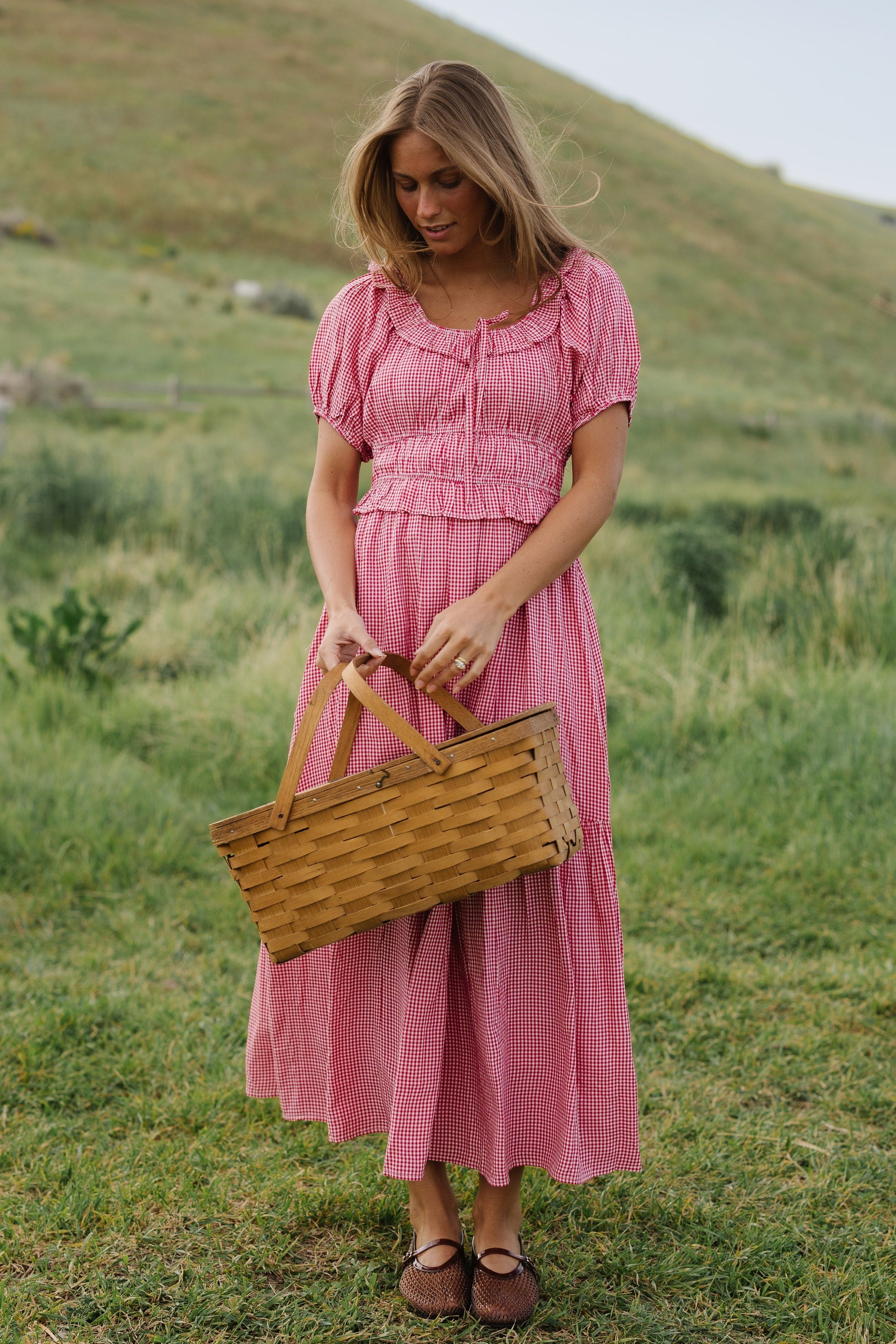 Young woman wearing a red and white gingham midi dress with a scoop neckline, wide waistband and a full skirt.