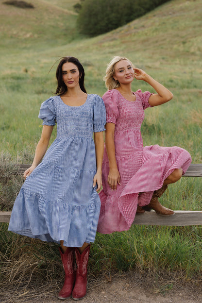 Two young woman wearing matching midi dresses in different colors.  One in red gingham and one in blue gingham.