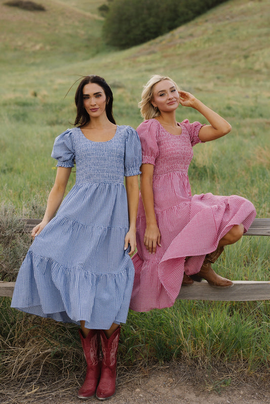 Two young woman wearing matching midi dresses in different colors.  One in red gingham and one in blue gingham.